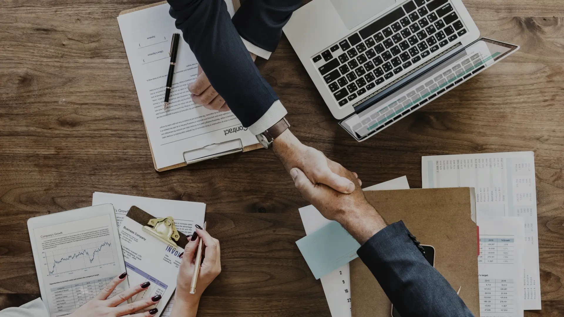 Two people shaking hands over contracts and business documents